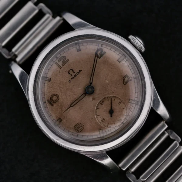 Displayed is the Omega WWII Era Military Sub Seconds wristwatch, featuring a metal link band and a weathered round dial. It has Arabic numerals at 3, 9, and 12 oclock with a small seconds subdial at 6 oclock on a striking black background.