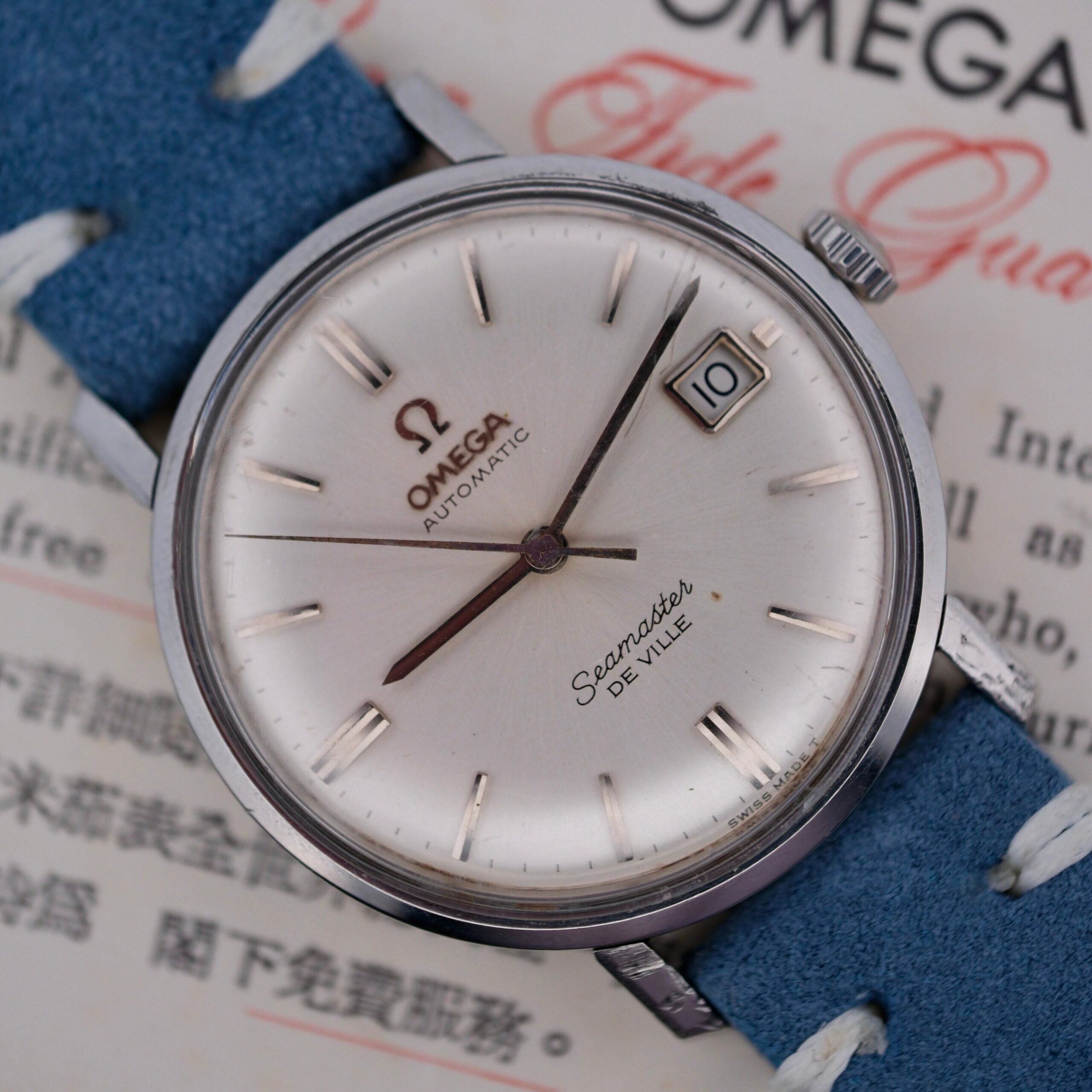 A close-up of the Omega Seamaster Deville Automatic for the Japanese Market showcases a silver dial with baton markers and a date display at 3 oclock. The watch features a blue leather strap, elegantly set against a background with text.
