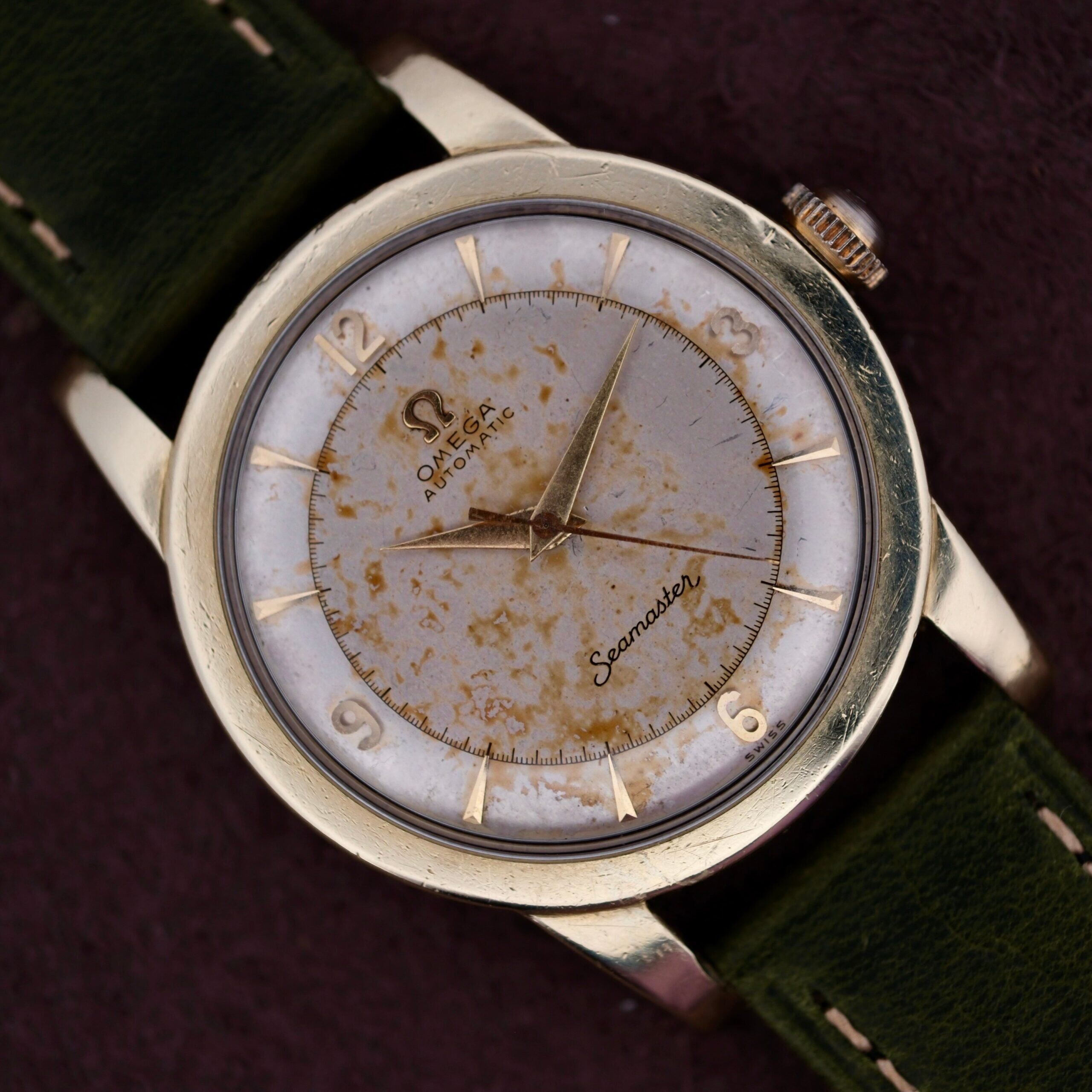The Omega Seamaster Gold Automatic 354 features a vintage gold case, weathered white dial, gold hour markers and hands, Omega Automatic and Seamaster markings, and an elegant green leather strap that enhances the timeless charm of the collection.