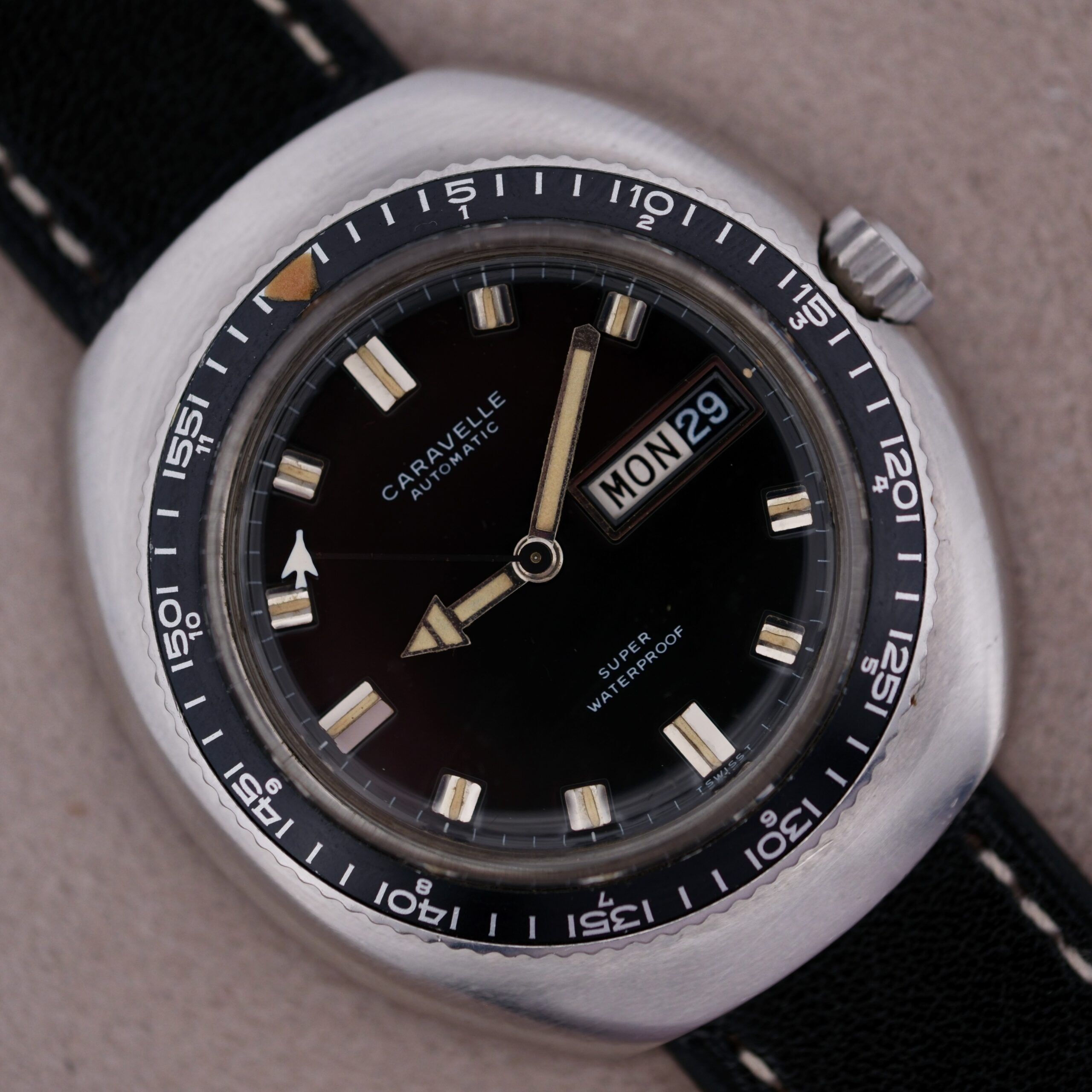 The vintage Caravelle Automatic Ref 745 Diver Jet Seconds wristwatch boasts a black dial displaying Mon 29, white hour markers, a rotating bezel with minute marks, and is attached to a black strap with white stitching. It proudly bears the label Super Waterproof.