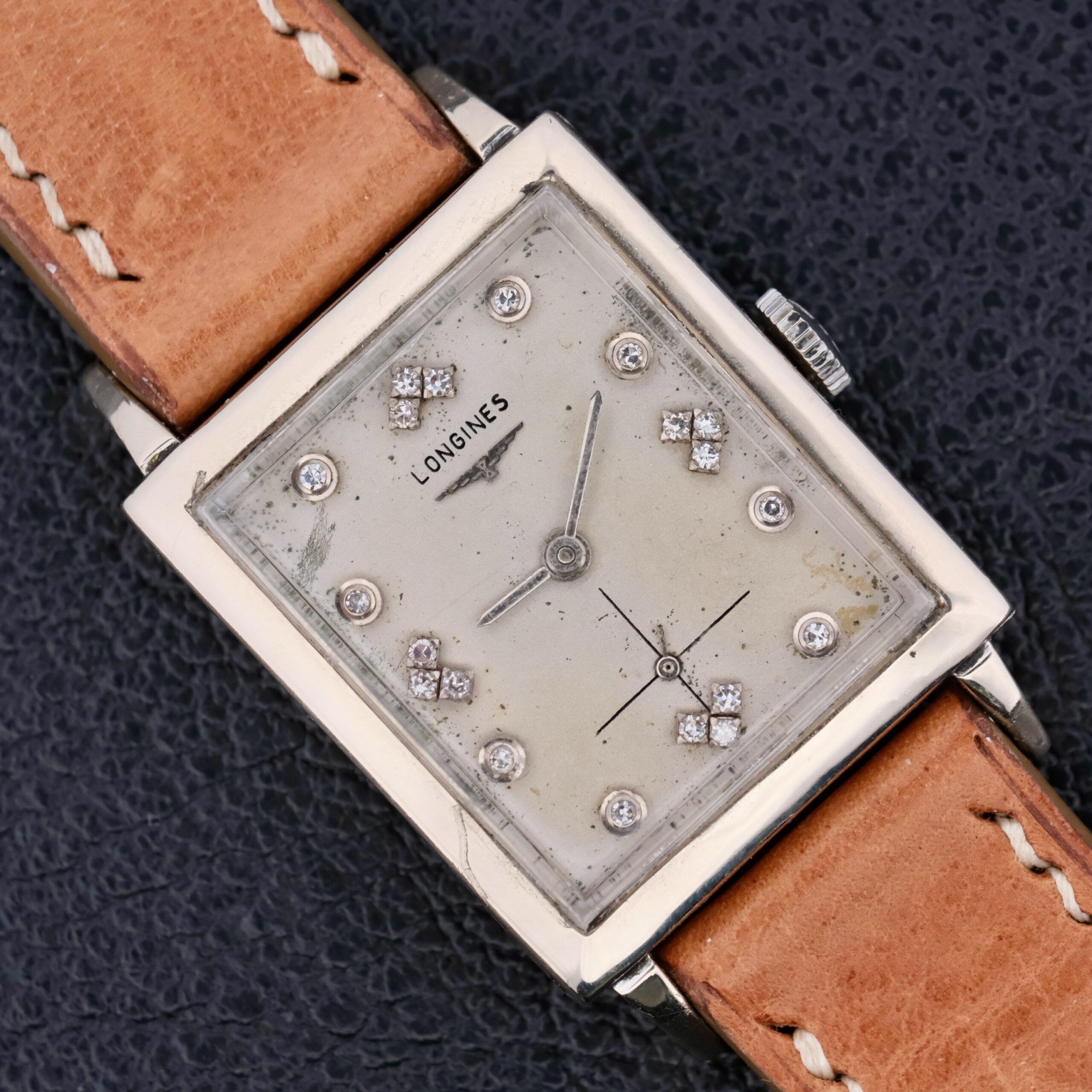 A vintage Longines Tank, 14k white gold watch with a silver rectangular case and light brown leather strap. The dial features a slightly aged look with diamond markers and the iconic Longines name below the 12 oclock position.