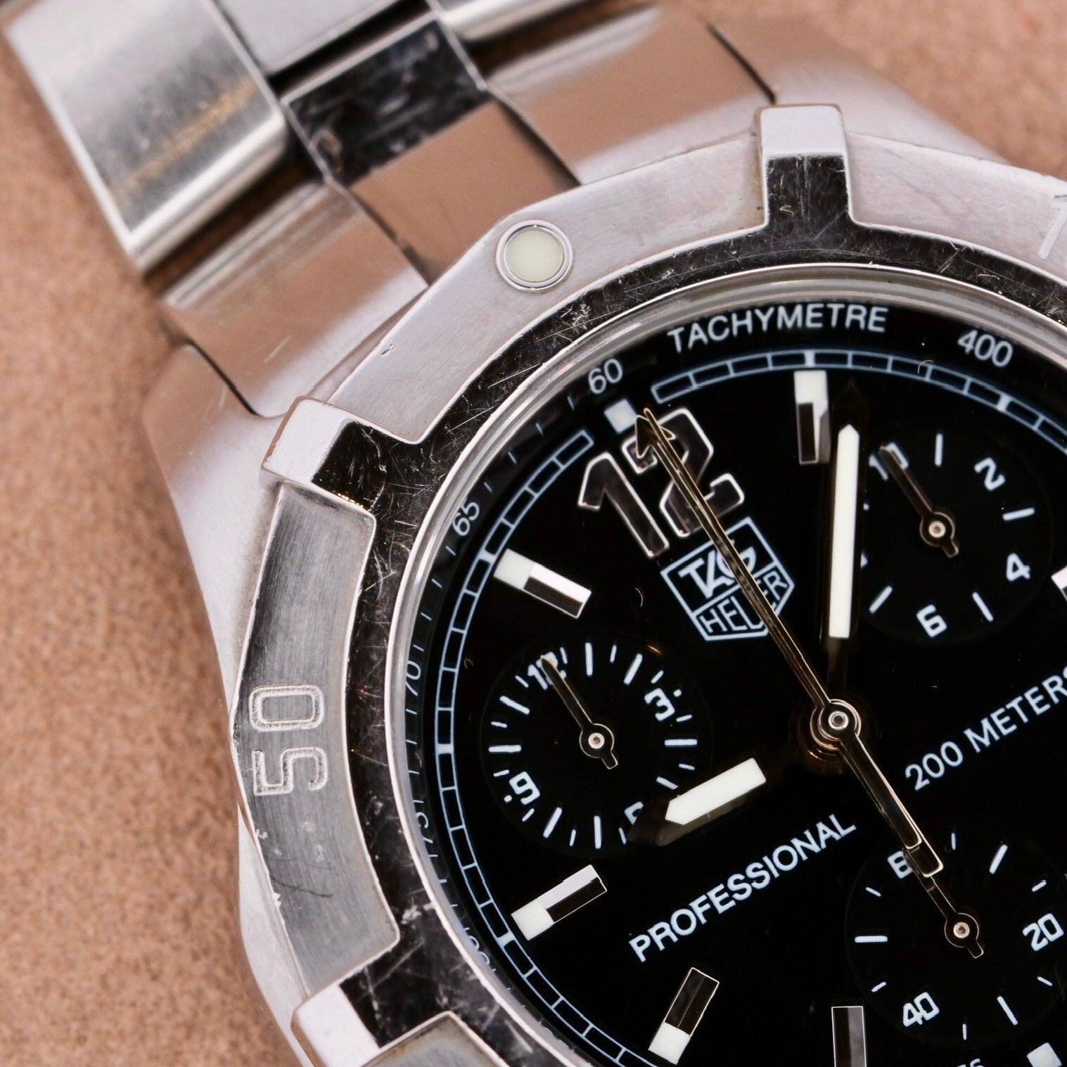 A detailed shot of the Tag Heuer 2000 Professional Chronograph with a metal bracelet; it features a black dial, three sub-dials, silver markers, and a tachymeter scale. It exemplifies precision with water resistance up to 200 meters.