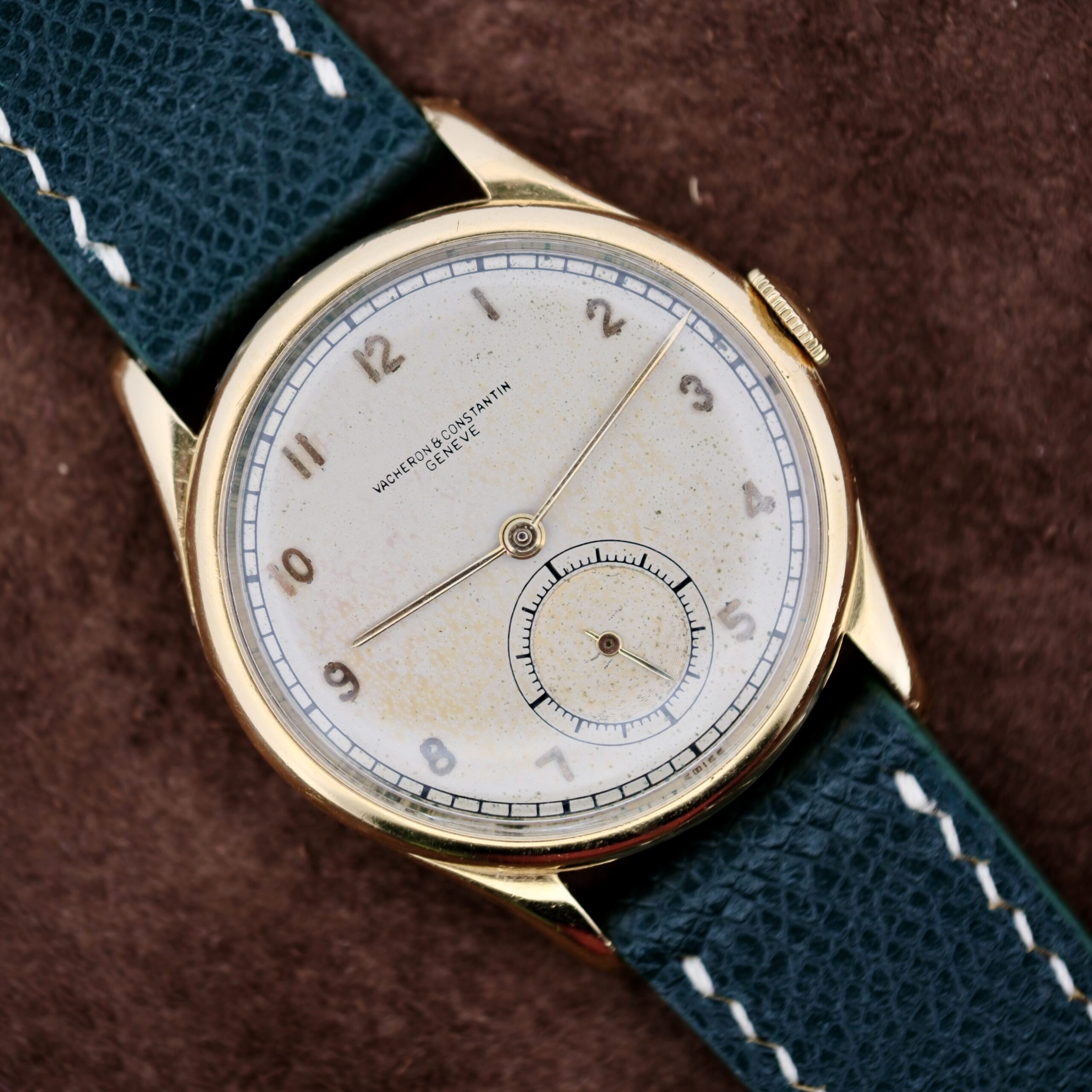 The 1940s Vacheron Constantin Caltrava V453 is a timeless vintage wristwatch featuring a gold case, subtly worn white dial with Arabic numerals, and a subdial at the 6 oclock position. The black leather strap with white stitching enhances its classic look, while the brand name stands proudly on the dial.