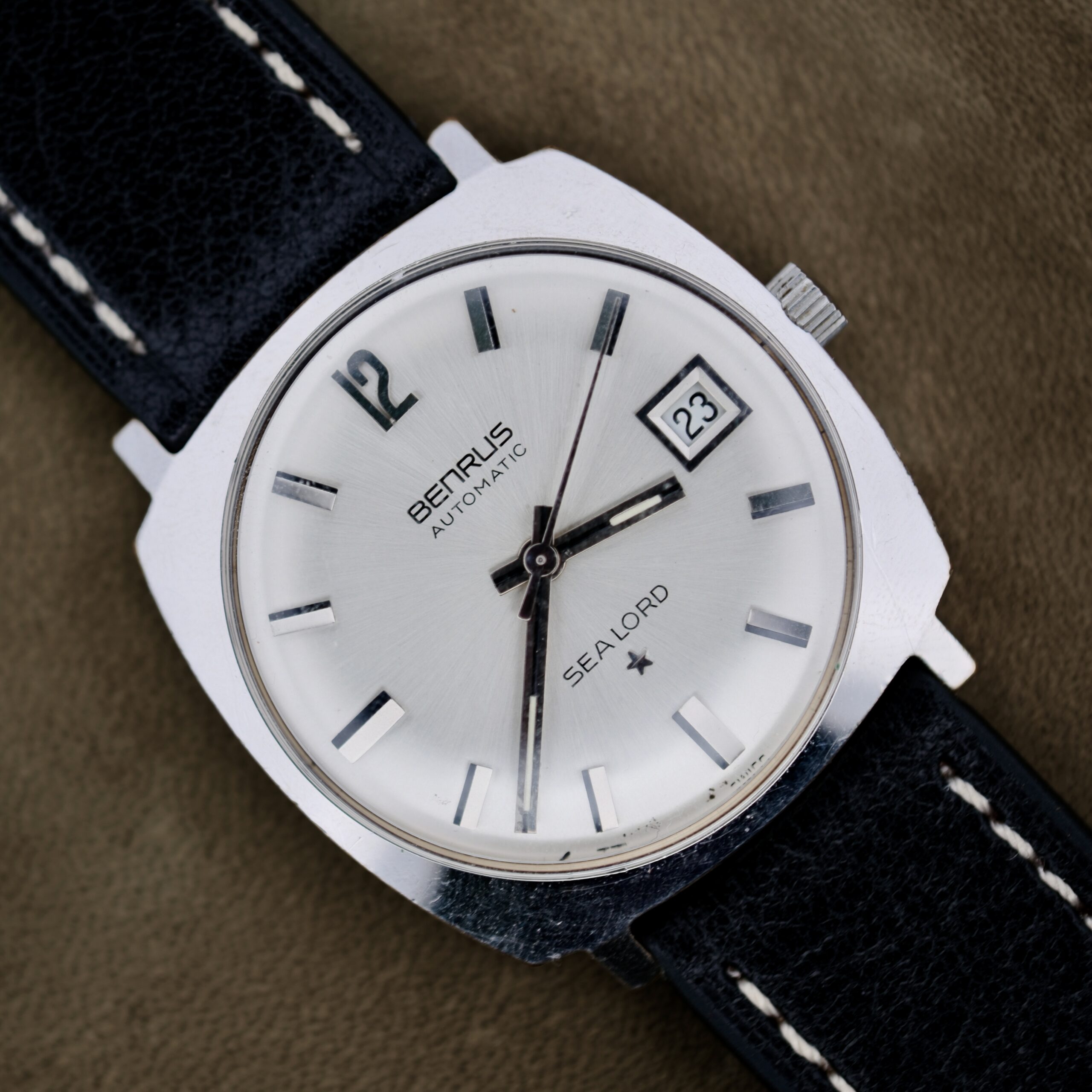 A close-up of a silver Benrus Automatic Sea Lord Date wristwatch with a black leather strap, silver dial, black hour markers, date display at 3 oclock, and black hour, minute, and second hands.