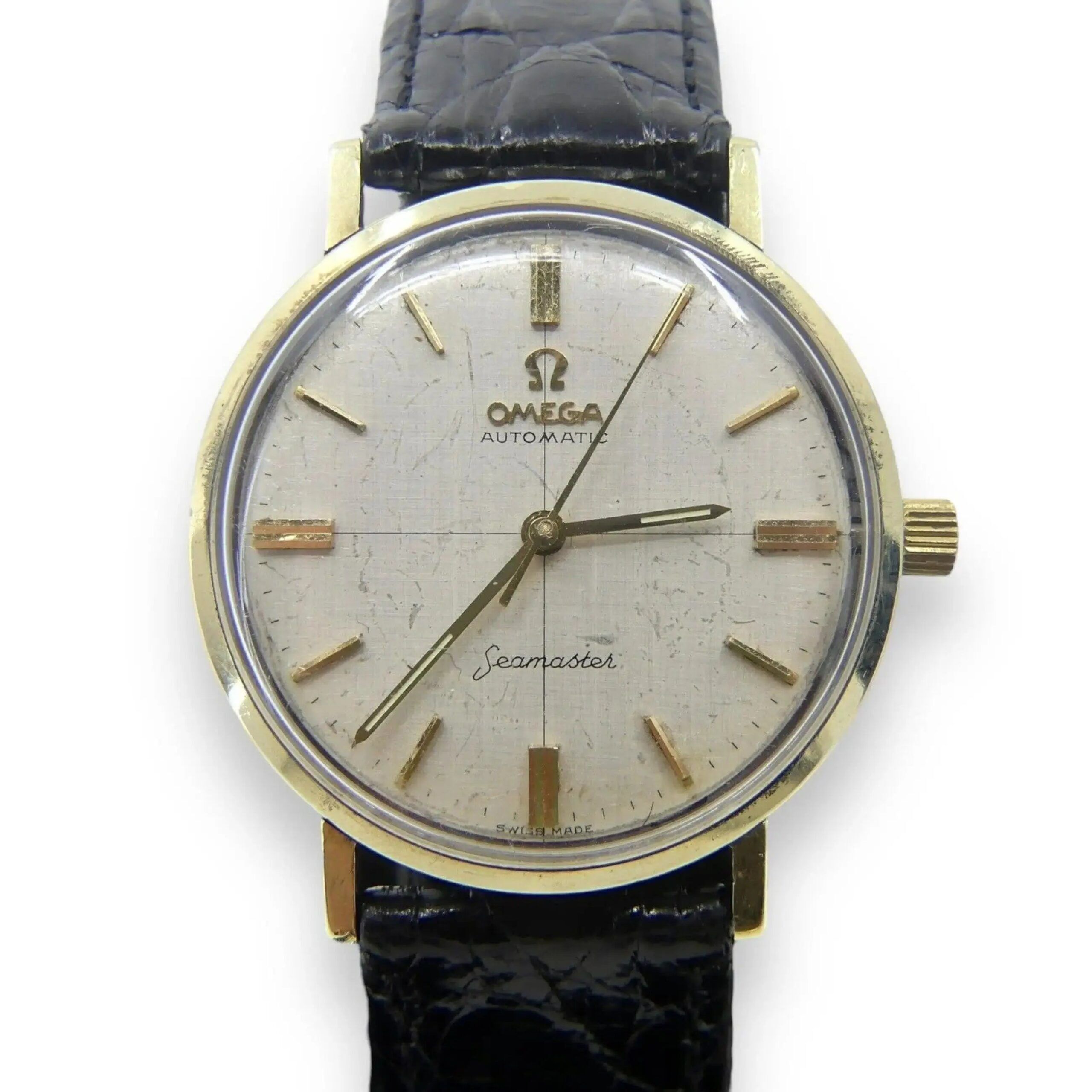 A vintage Omega Seamaster Deville mens watch with a gold-tone case, textured white dial, gold hour markers and hands, and the Omega logo. It features Seamaster inscribed and comes with a black leather strap. Includes box and papers.